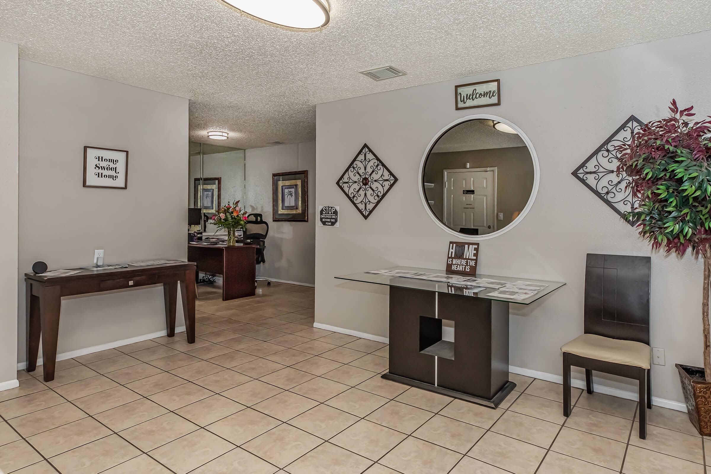 Modern living room with tiled flooring and decorative wall mirror at Wood River Apartments in Corpus Christi, Texas