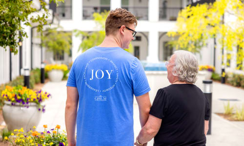 Two people walking together in a garden at Barclay House of Oakleaf Village in Lexington, South Carolina