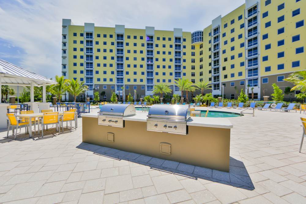 Resort-style pool area with grilling station and lounge chairs surrounded by palm trees at Bayview Student Living in North Miami, Florida