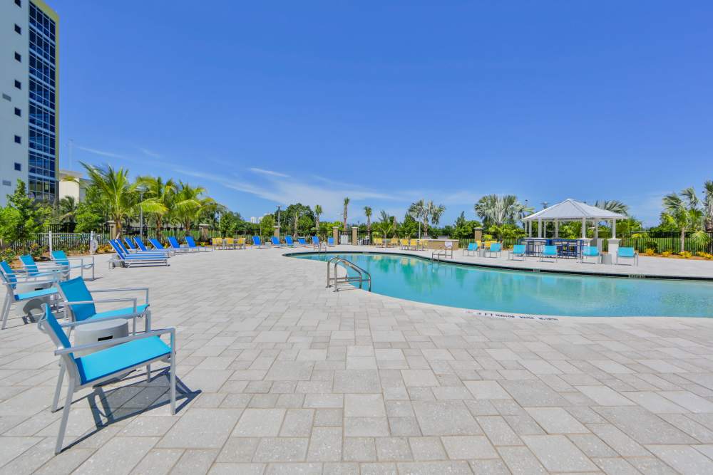 Resort-style swimming pool with lounge chairs and shaded cabana surrounded by palm trees at Bayview Student Living in North Miami, Florida