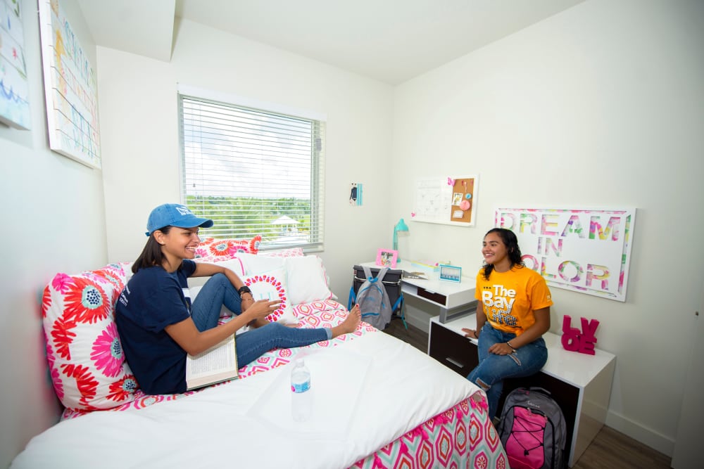 Two young women sitting on a brightly decorated bed in a cozy, well-lit bedroom at Bayview Student Living in North Miami, Florida