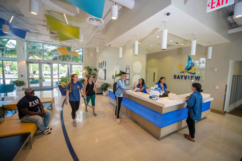 Bright, welcoming lobby with staff assisting residents and visitors, modern decor, and tropical plants at Bayview Student Living in North Miami, Florida
