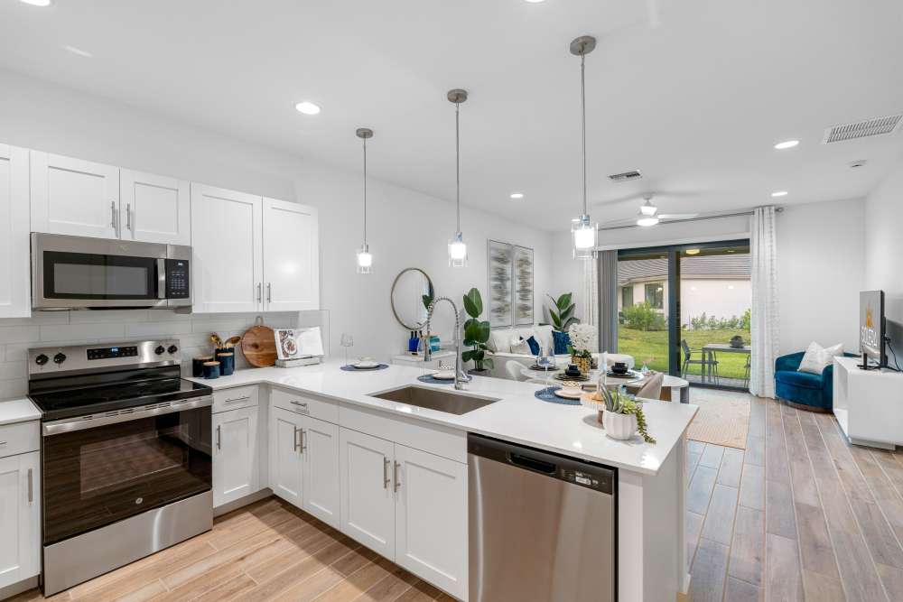 Modern kitchen with stainless steel appliances, granite countertops, and open layout leading to patio area at Solera at Avalon Trails in Delray Beach, Florida