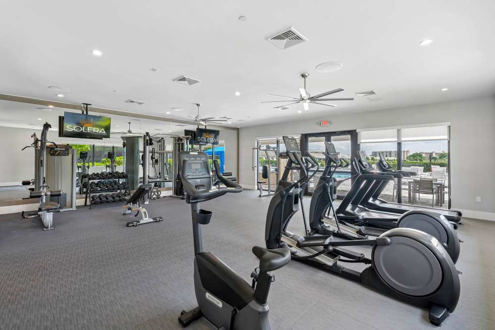 Modern fitness center with cardio machines, weights, large windows, and outdoor views at Solera at Avalon Trails in Delray Beach, Florida