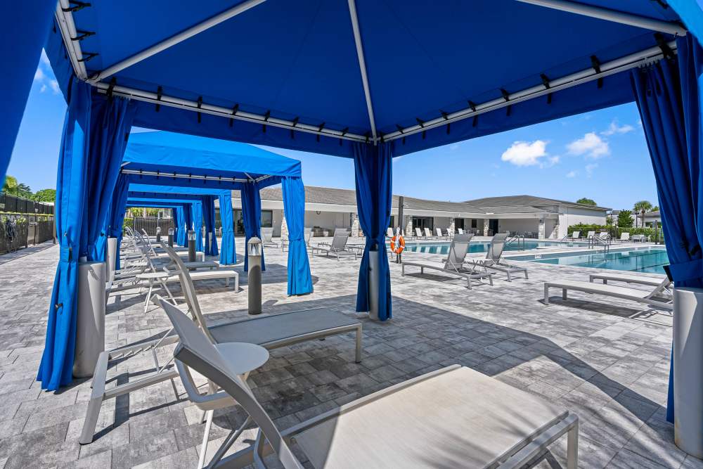 Resort-style pool area with blue cabanas and lounge chairs under sunny skies at Solera at Avalon Trails in Delray Beach, Florida