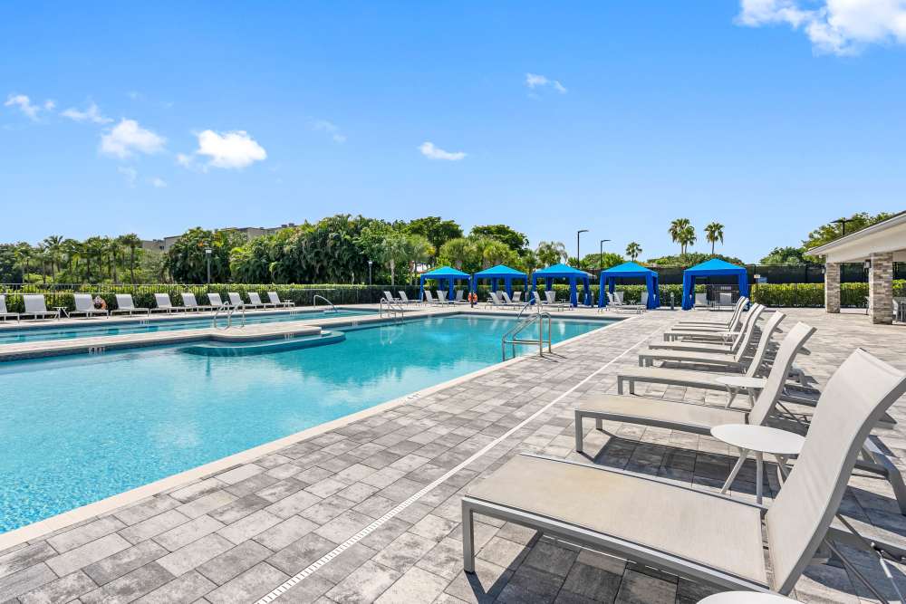 Resort-style sparkling pool surrounded by lounge chairs and blue cabanas under a clear sky at Solera at Avalon Trails in Delray Beach, Florida