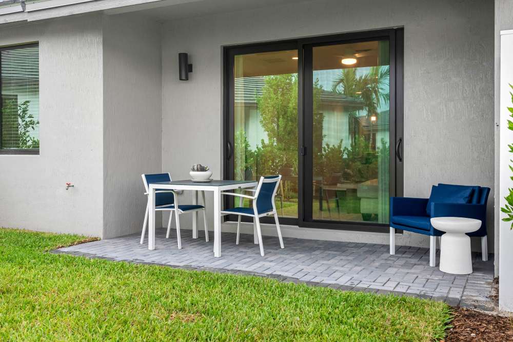 Patio area with a dining table, blue chairs, and a cozy accent chair surrounded by greenery at Solera at Avalon Trails in Delray Beach, Florida