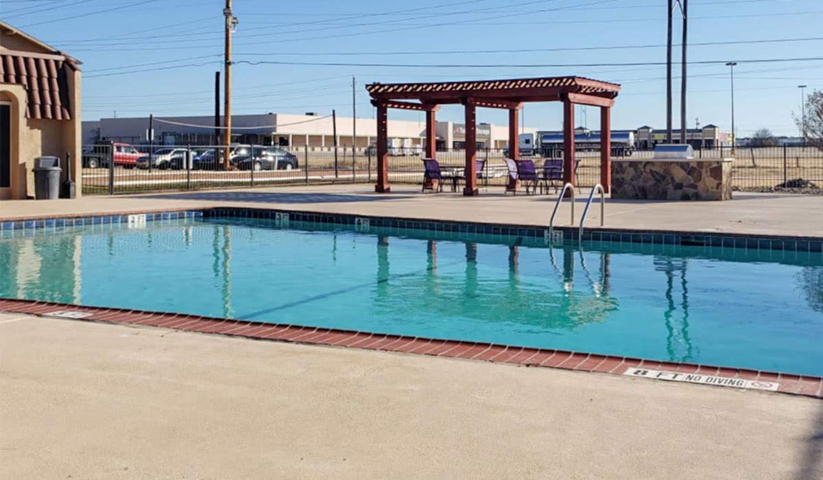 Sparkling pool with surrounding patio and shaded seating area in a gated community at Riatta Ranch Apartments in Abilene, Texas