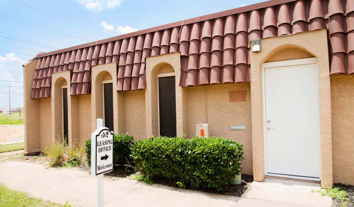 Leasing office exterior with welcoming sign and lush greenery in front at Riatta Ranch Apartments in Abilene, Texas