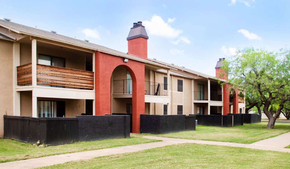 Two-story apartment building with balconies and fenced yards in a green landscape at Riatta Ranch Apartments in Abilene, Texas