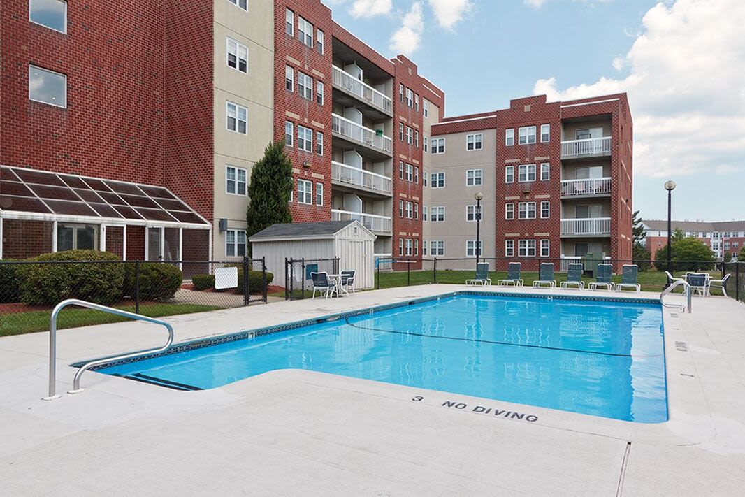 Resort-style swimming pool with lounge chairs surrounded by apartment building at Anchors Weigh in Chelsea, Massachusetts