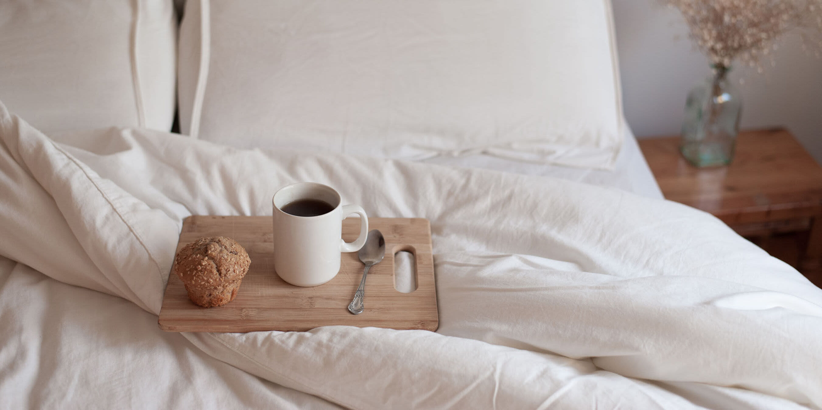  A white mug filled with coffee and a muffin sit on a wooden tray on a white bed at Peterborough Apartments in Boston, Massachusetts