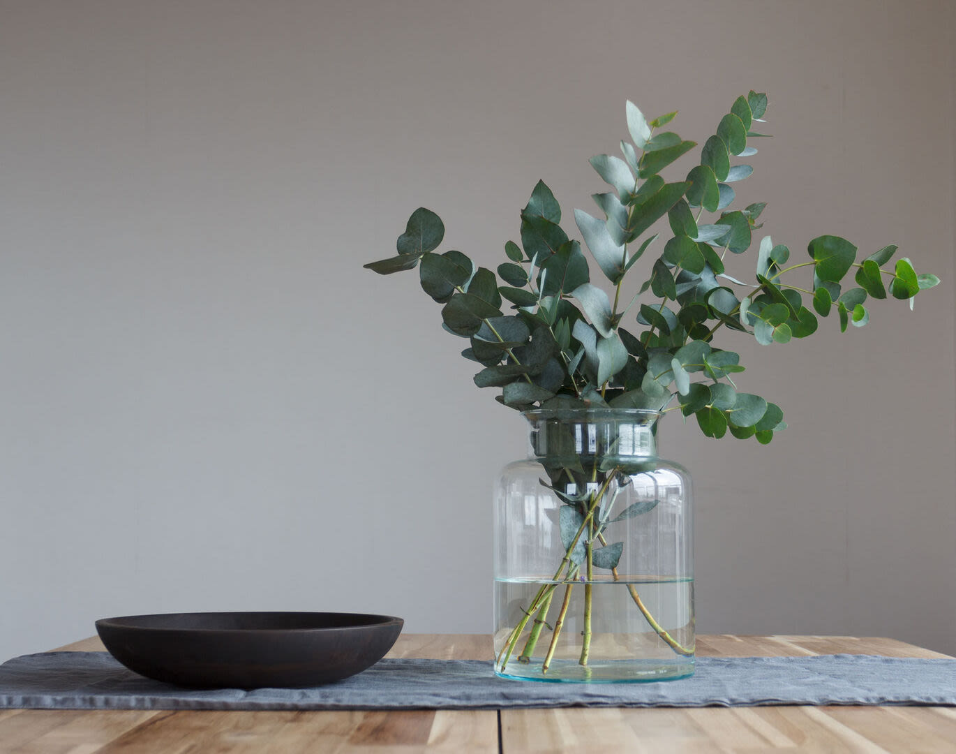 A glass vase filled with eucalyptus branches sits on a wooden table next to a black bowl at Peterborough Apartments in Boston, Massachusetts