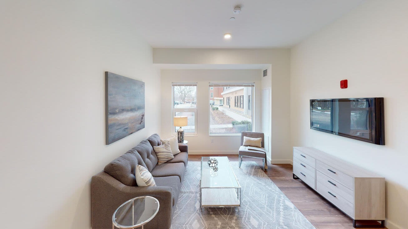 Cozy living room with couch, chair, coffee table and window at The Mcelwain School Apartments in Bridgewater,Massachusetts