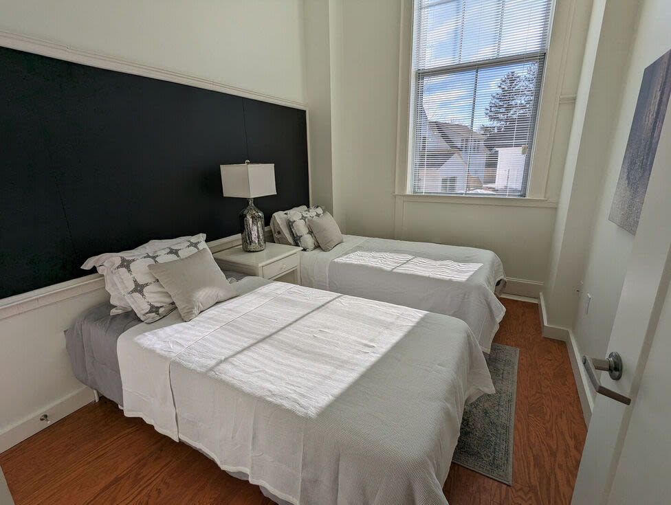 Bedroom with two beds, grey sheets and window at The Mcelwain School Apartments in Bridgewater,Massachusetts