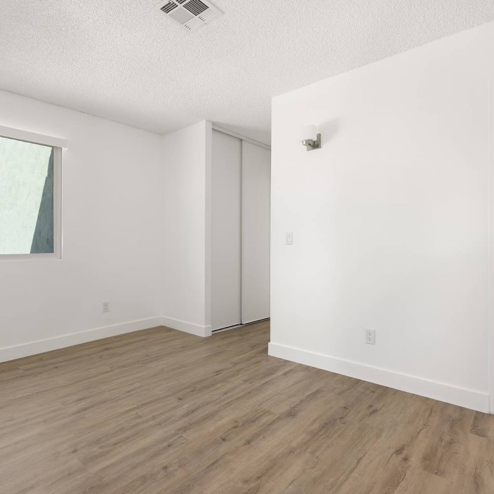Empty room with wooden floor, window, and open door to a bathroom at Valle at Mission in Escondido, California