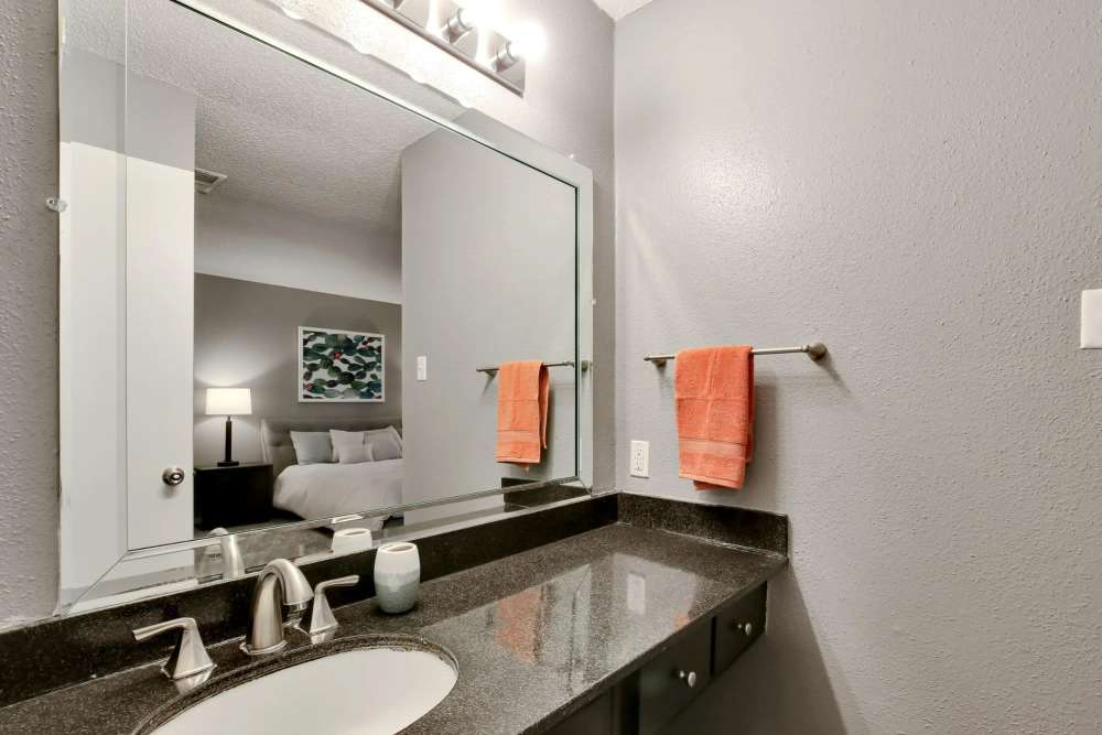 Bright bathroom with dark marble countertop, large mirror and stainless-steel sink at Parkwyn Townhomes in North Richland Hills,Texas