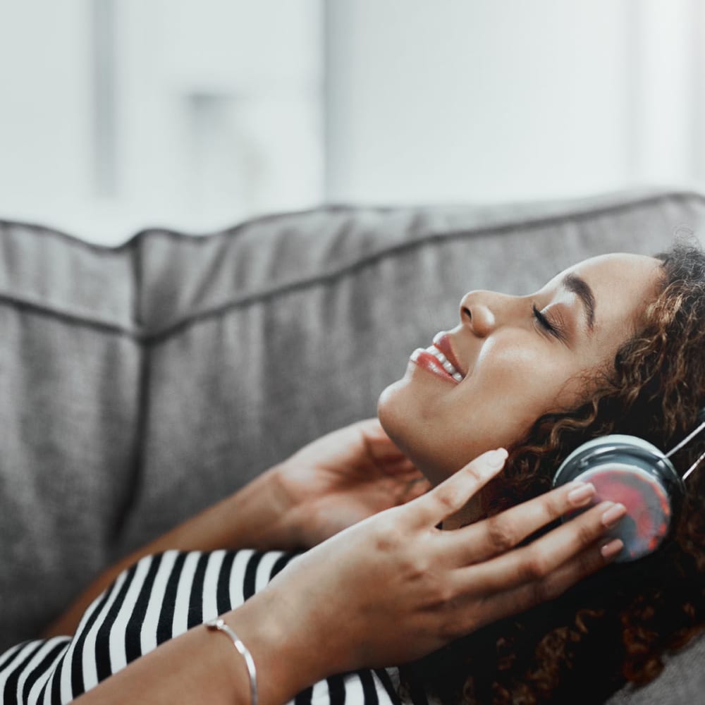 Resident listening to her favorite artist on headphones from the comfort of her couch at Oaks 5th Street Crossing at City Station in Garland, Texas