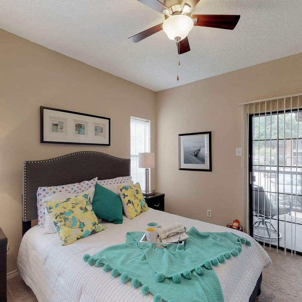 Model apartment's primary bedroom with plush carpeting and a ceiling fan at Oaks Hackberry Creek in Las Colinas, Texas