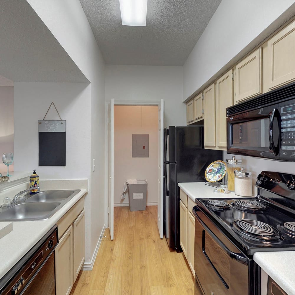 Wood-style flooring and black appliances in a model home's kitchen at Oaks Hackberry Creek in Las Colinas, Texas