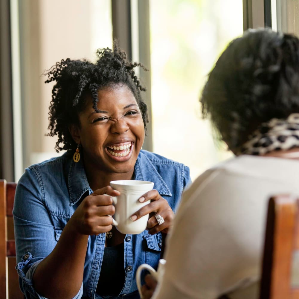 Friends laughing together over a cup of coffee near Vidorra McKinney Avenue in Dallas, Texas