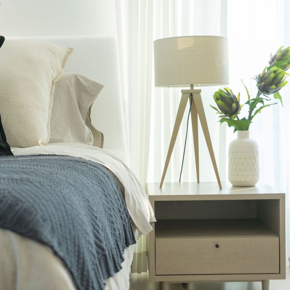 Comfortably decorated bed and adjacent nightstand with a lamp and plant in a model apartment at Sage at Cypress Cay in Lutz, Florida