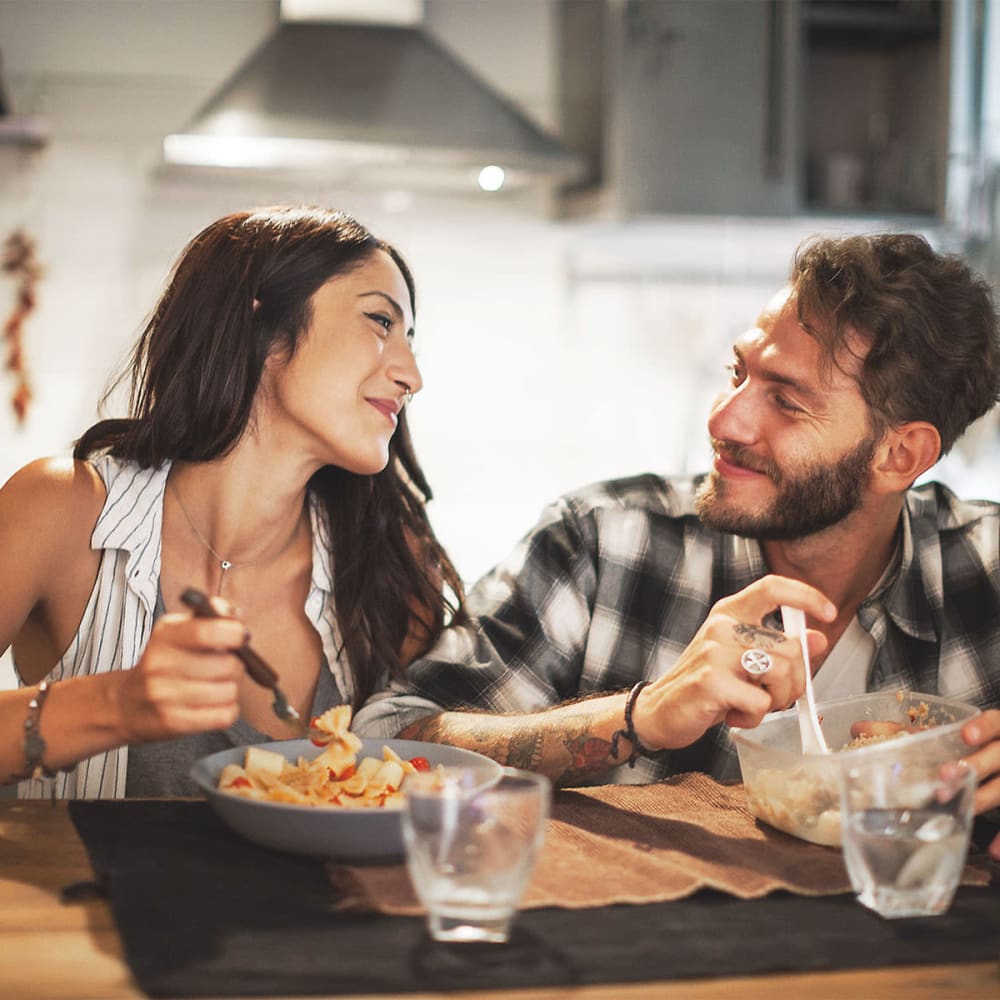 Happy resident couple smiling at each other and enjoying a meal together in the kitchen of their new home at Mission Rock at San Rafael in San Rafael, California