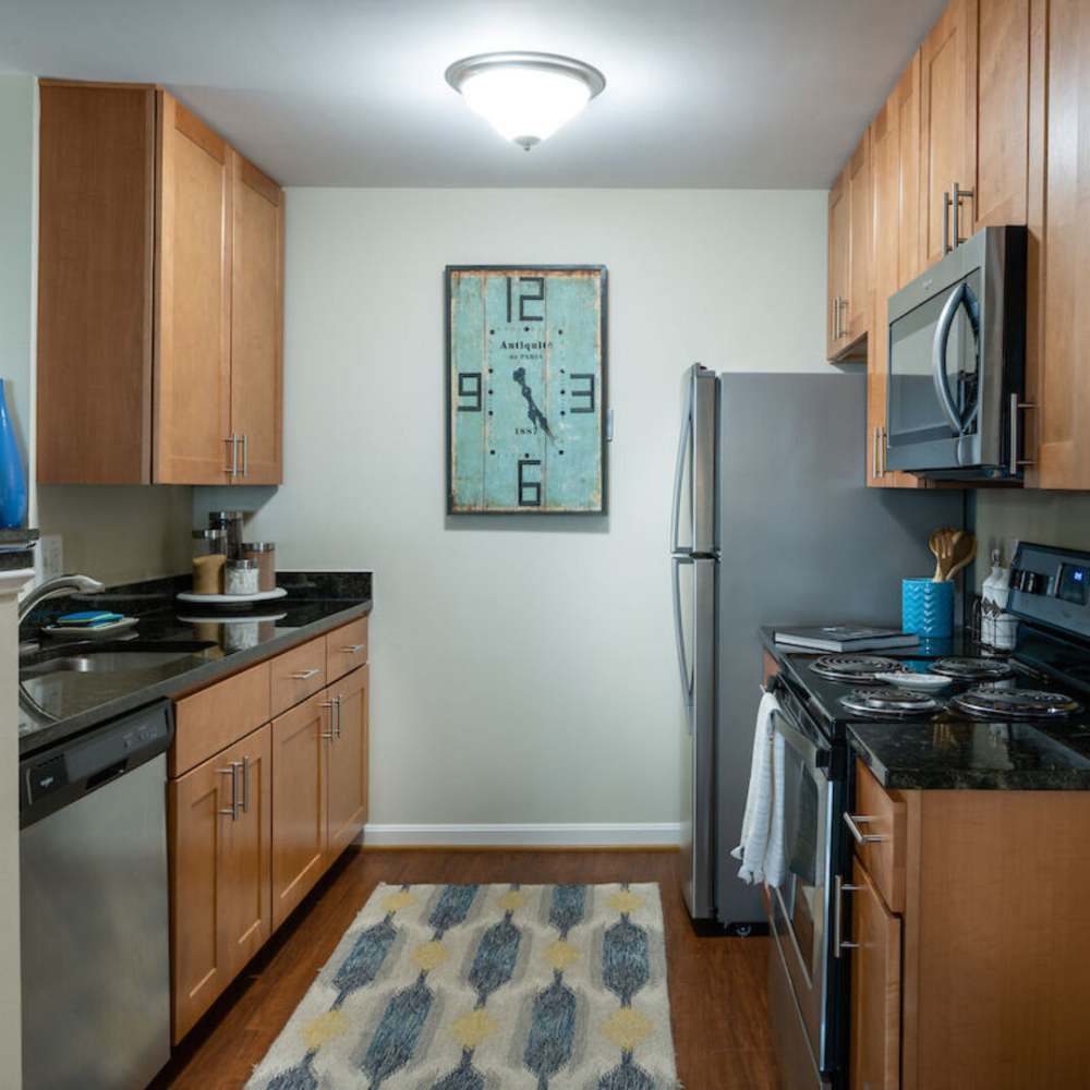 Apartment kitchen with stainless steel appliances and wooden cabinetry wall clock at The Elms at Oakton in Fairfax, Virginia