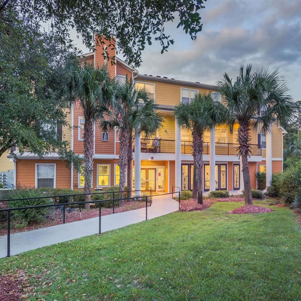 Exterior of the community clubhouse with a paved walkway lined by palm trees at Evergreens at Mahan in Tallahassee, Florida