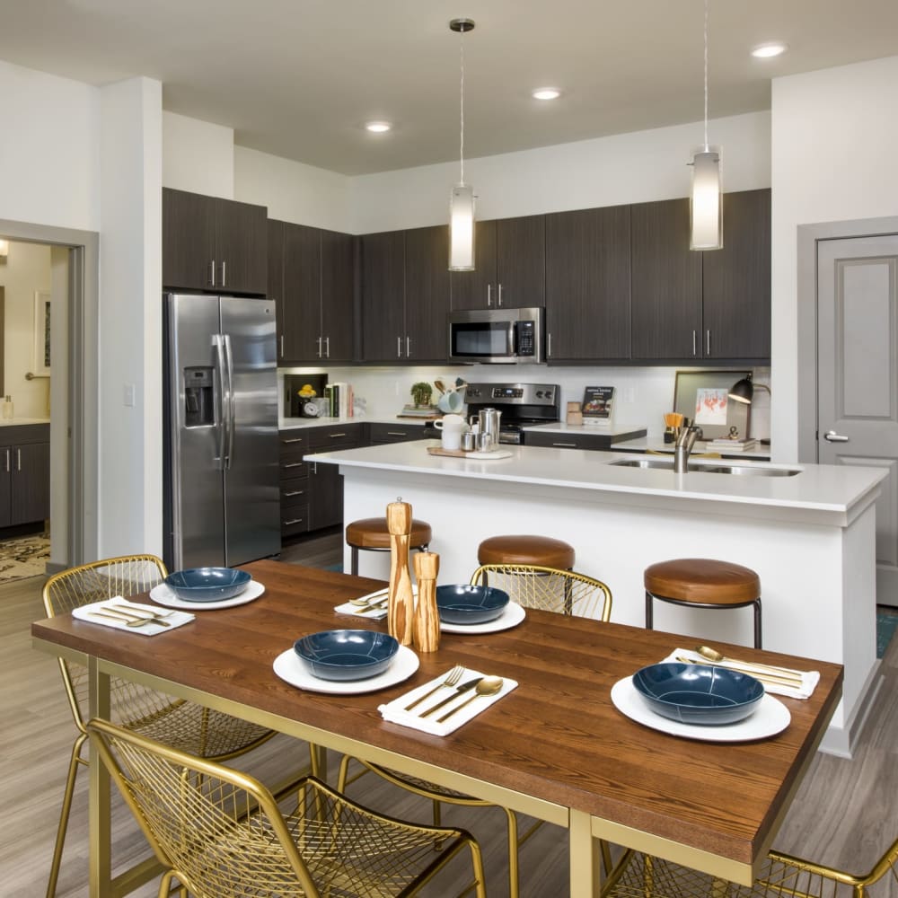 A set dining room table next to the kitchen and island in an apartment at Ravella at Town Center in Jacksonville, Florida