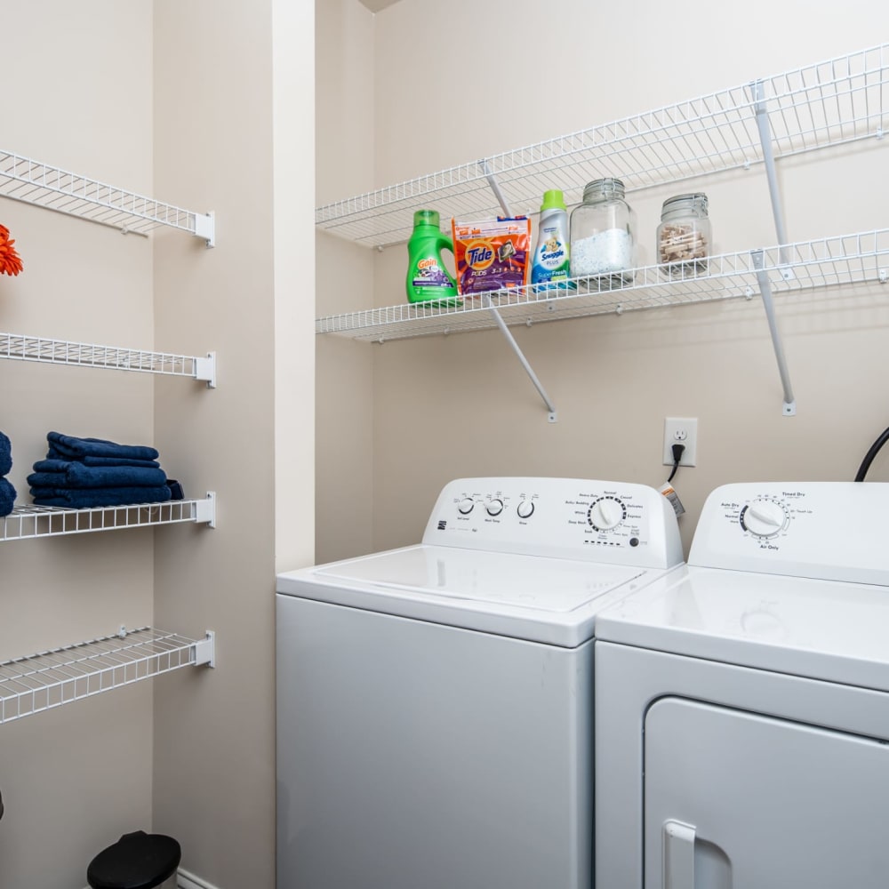 A full sized washer and dryer in an apartment laundry room with shelving at Riverstone in Macon, Georgia