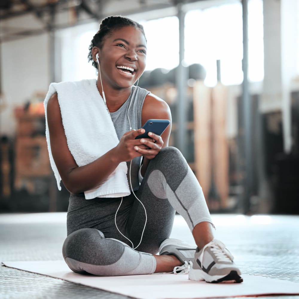 A woman smiling at her phone while on a yoga mat in the fitness center at The Lively Indigo Run in Ladson, South Carolina