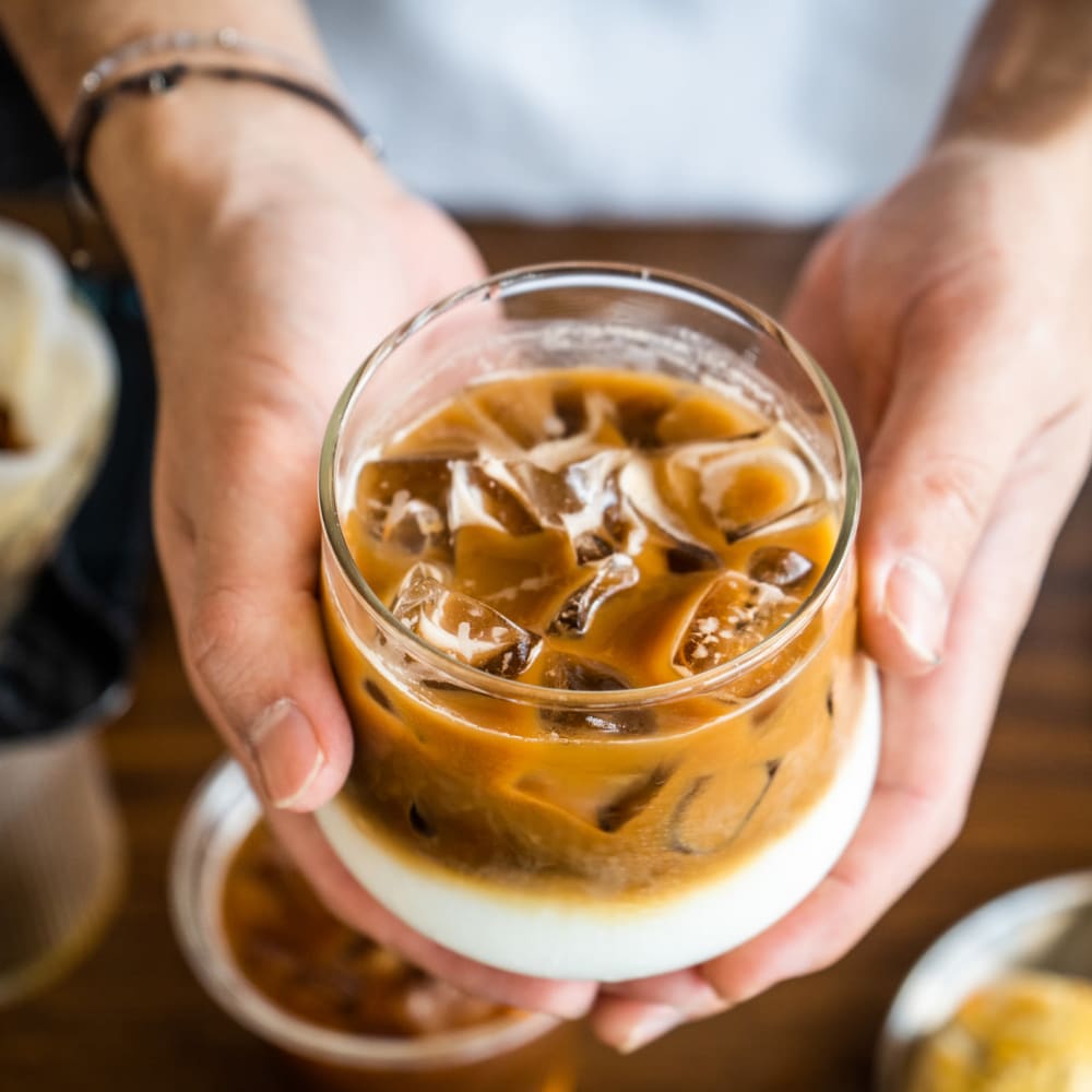 Hands holding a cup of iced coffee near Dolphin Marina Apartments in Marina Del Rey, California