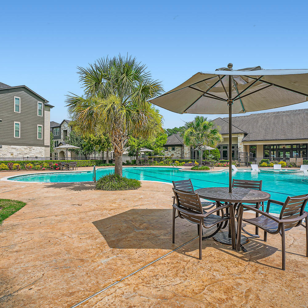 Poolside table and chairs with covered umbrella at Discovery at Kingwood in Kingwood, Texas