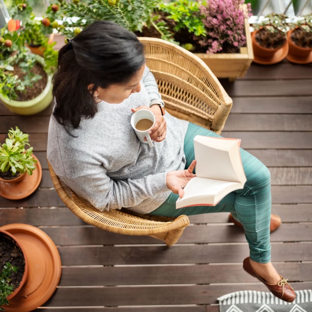 Resident reading with a cup of coffee on her balcony at Vista Creek Apartments in Castro Valley, California