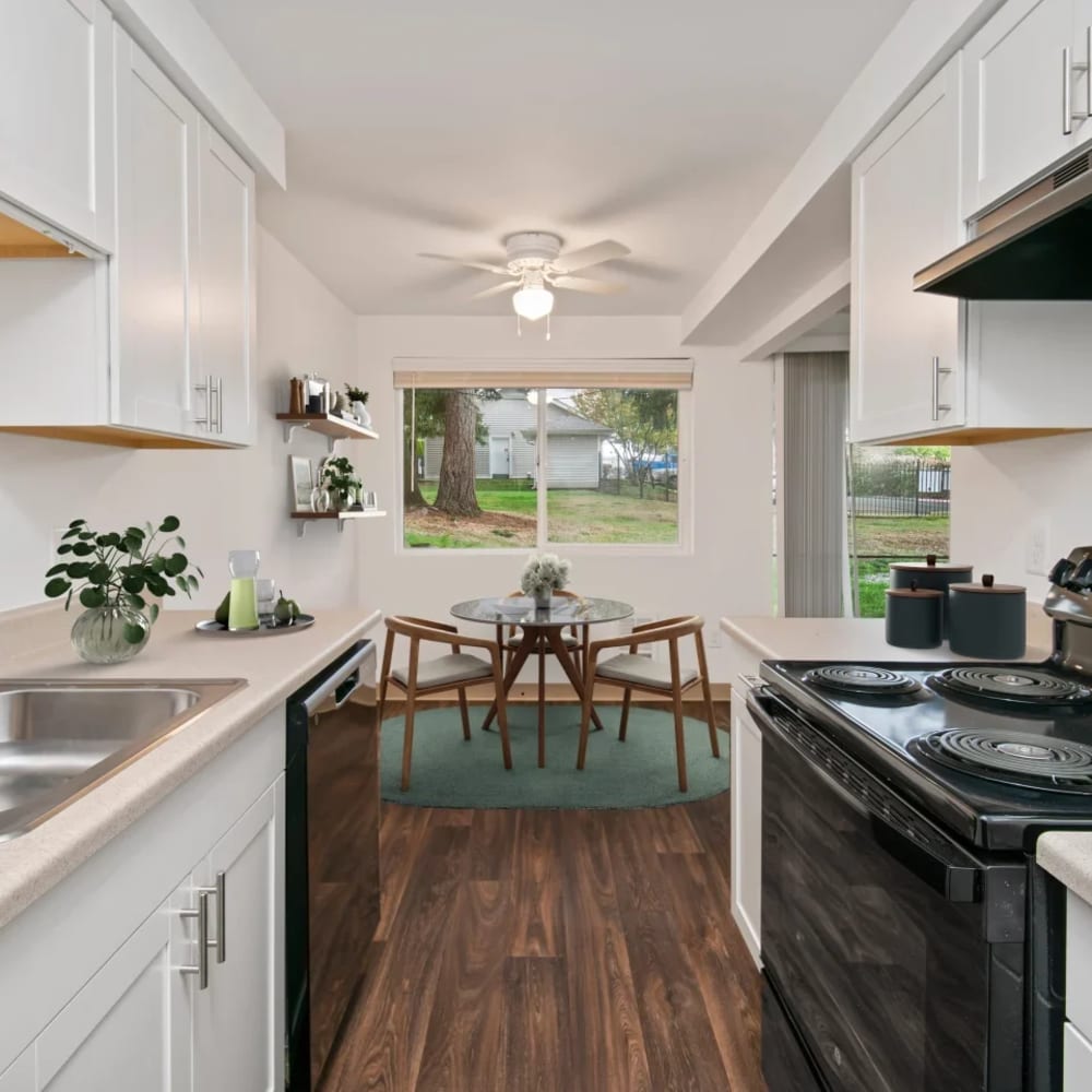 Galley kitchen and dining area of a model apartment home with wood-style flooring at Bluffs at Evergreen in Everett, Washington