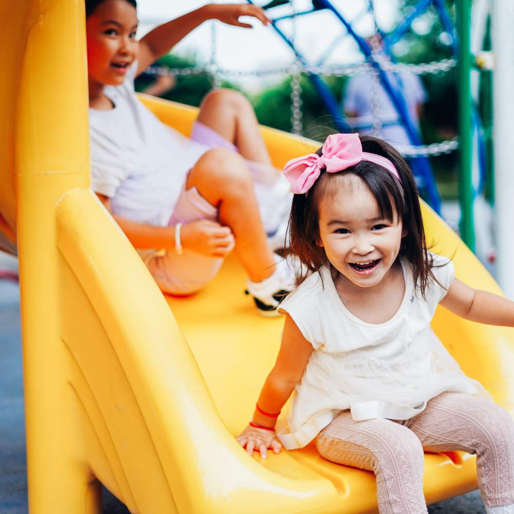 Child reaching the bottom of the slide with a smile on her face at the onsite children's playground at Sharps & Flats Apartment Homes in Davis, California