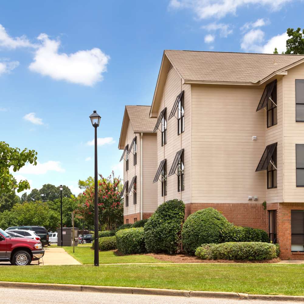 Exterior view of the apartment building surrounded by greenery and a car parked at The Arbors On Taylor in Montgomery, Alabama