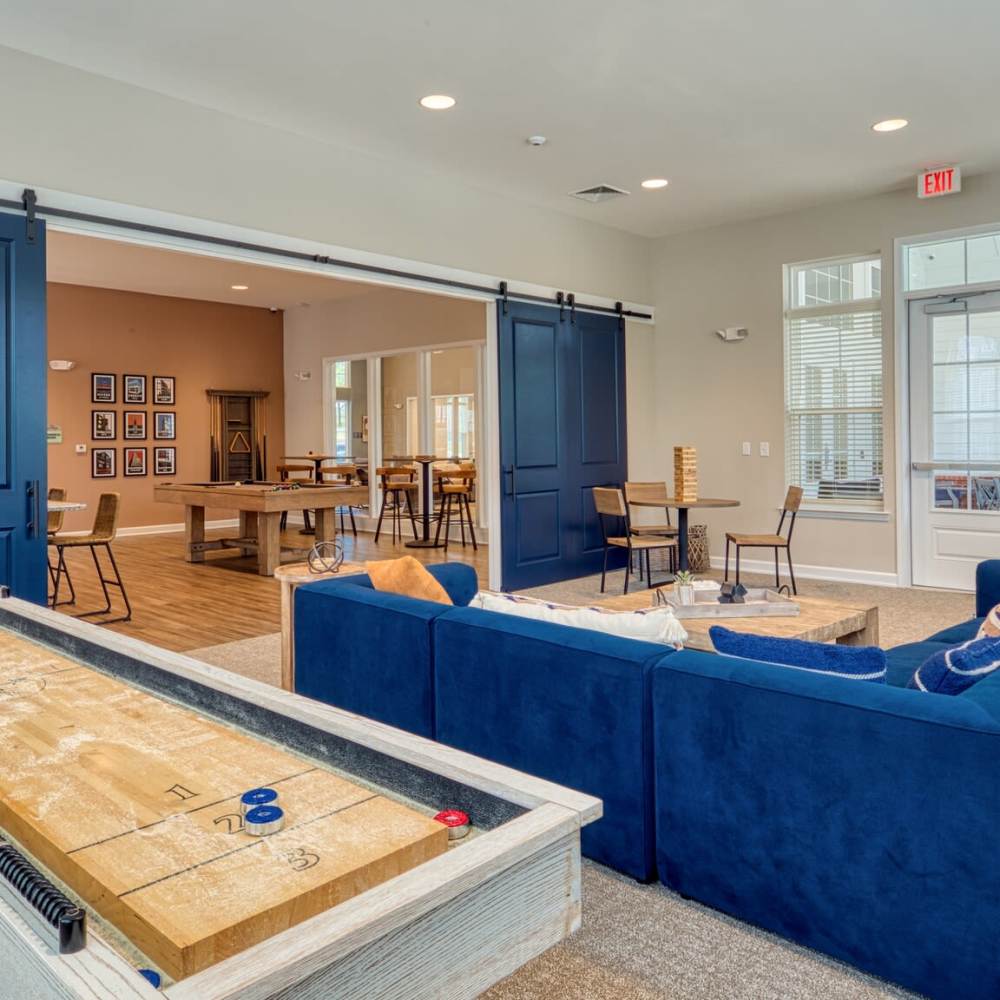 Recreation room with a shuffleboard table, blue sectional sofa, large windows, and sliding barn doors at Commonwealth Apartments in Midlothian, Virginia