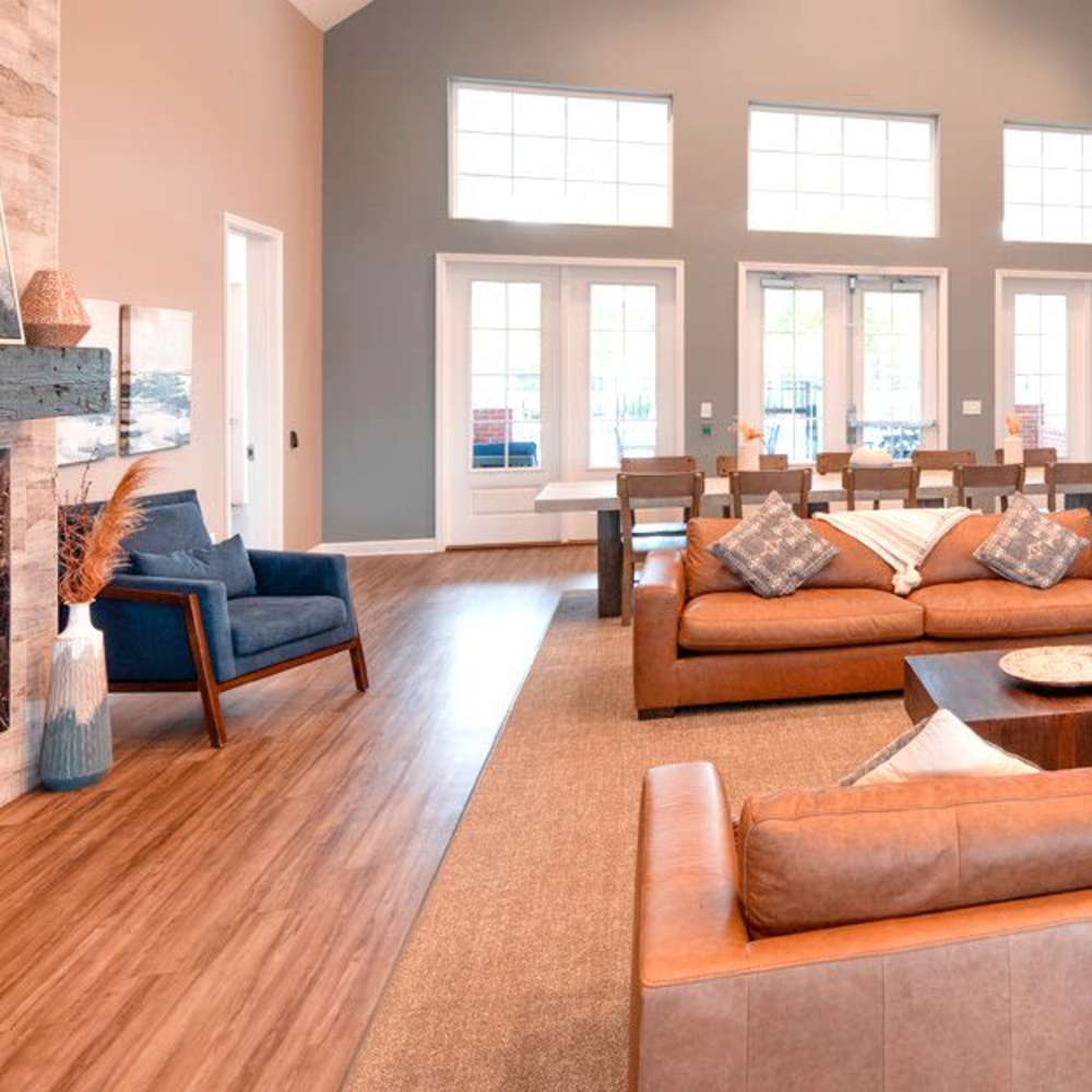 A spacious living room with leather sofas, a fireplace, and large windows at Commonwealth Apartments in Midlothian, Virginia