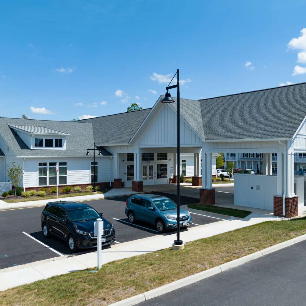 A modern, single-story building with a gable roof, white siding, and a covered entrance. Several parked cars and lampposts are in front of the building at Commonwealth Apartments in Midlothian, Virginia