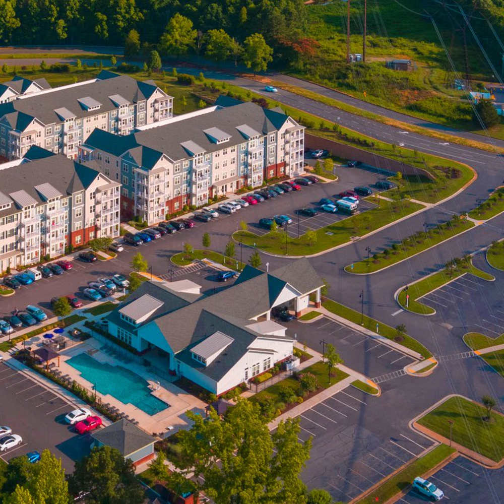 Aerial view of a residential complex with apartment buildings, parking lots, a pool, and surrounding greenery at Commonwealth Apartments in Midlothian, Virginia