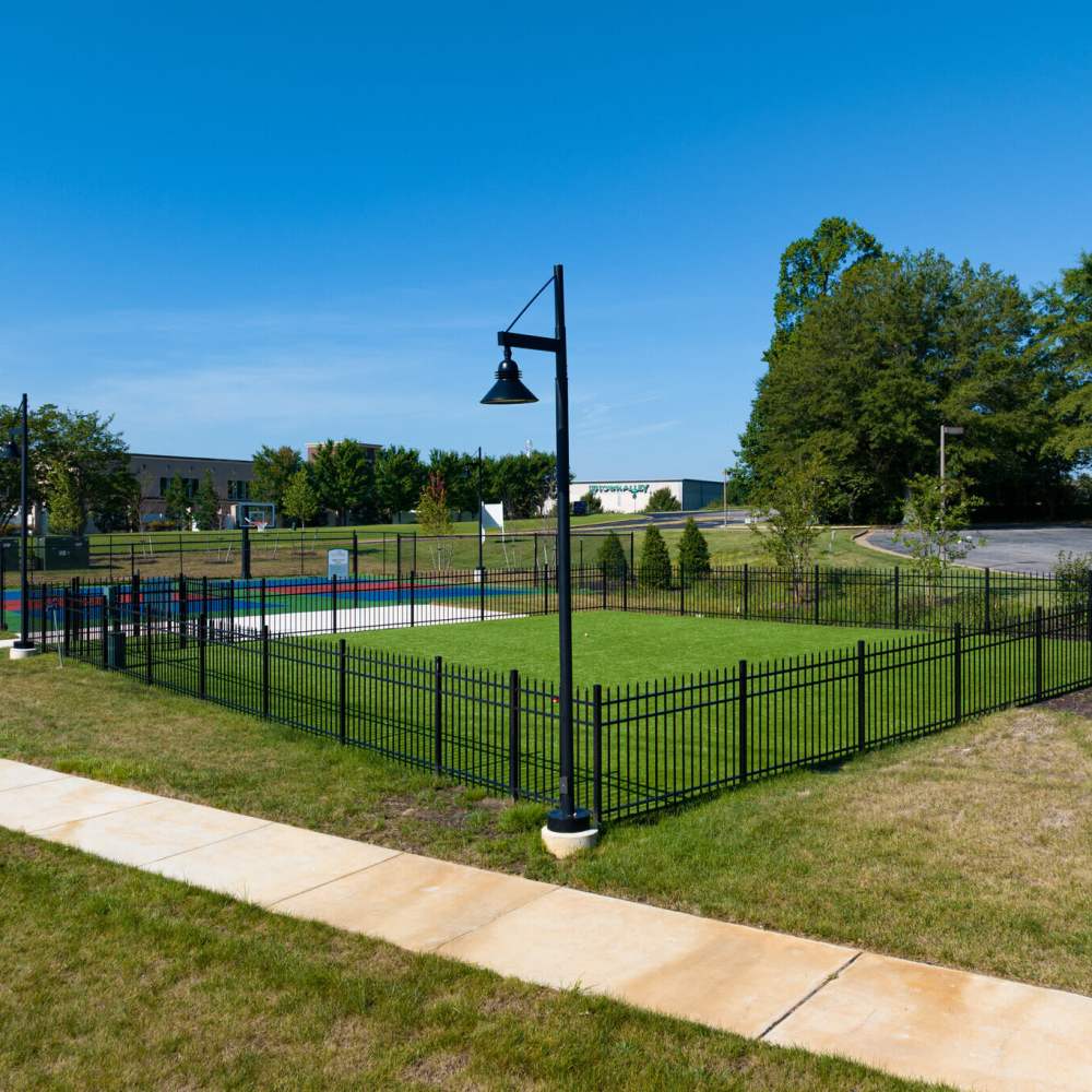 Enclosed grassy area beside a basketball court with lamp posts and surrounding trees at Commonwealth Apartments in Midlothian, Virginia