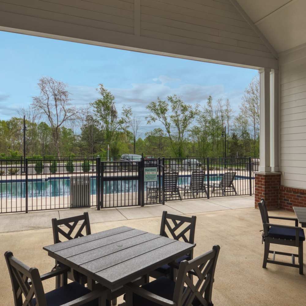 Patio with tables and chairs overlooking a fenced swimming pool surrounded by trees at Commonwealth Apartments in Midlothian, Virginia