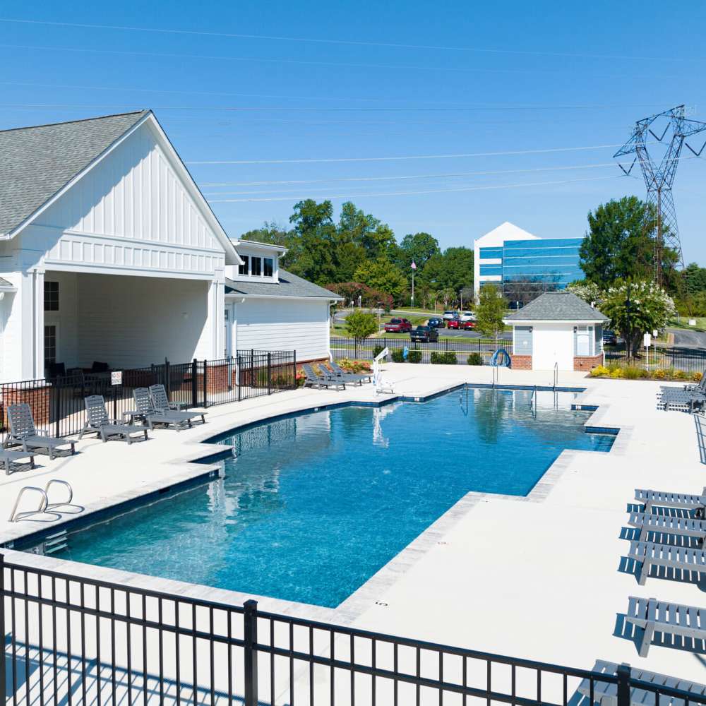 Outdoor pool with surrounding lounge chairs and white buildings under a clear blue sky at Commonwealth Apartments in Midlothian, Virginia