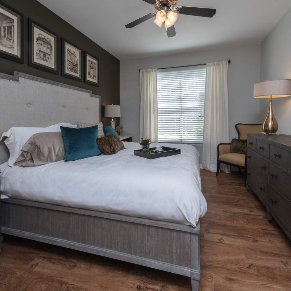 Well-lit bedroom with ceiling fan, large window, and hard-wood style flooring at Avonlea On The River in Duluth, Georgia