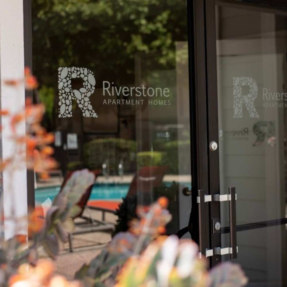 Entrance to Riverstone Apartment Homes with logo and view of the pool area through the glass door at Riverstone Apartments in Sacramento, California