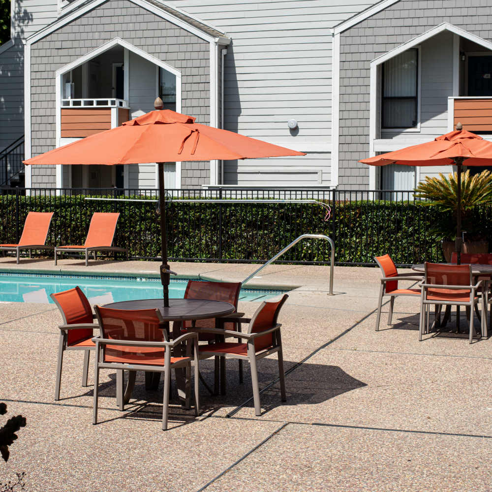 Outdoor dining area with tables and umbrellas near the pool at Riverstone Apartment Homes at Riverstone Apartments in Sacramento, California