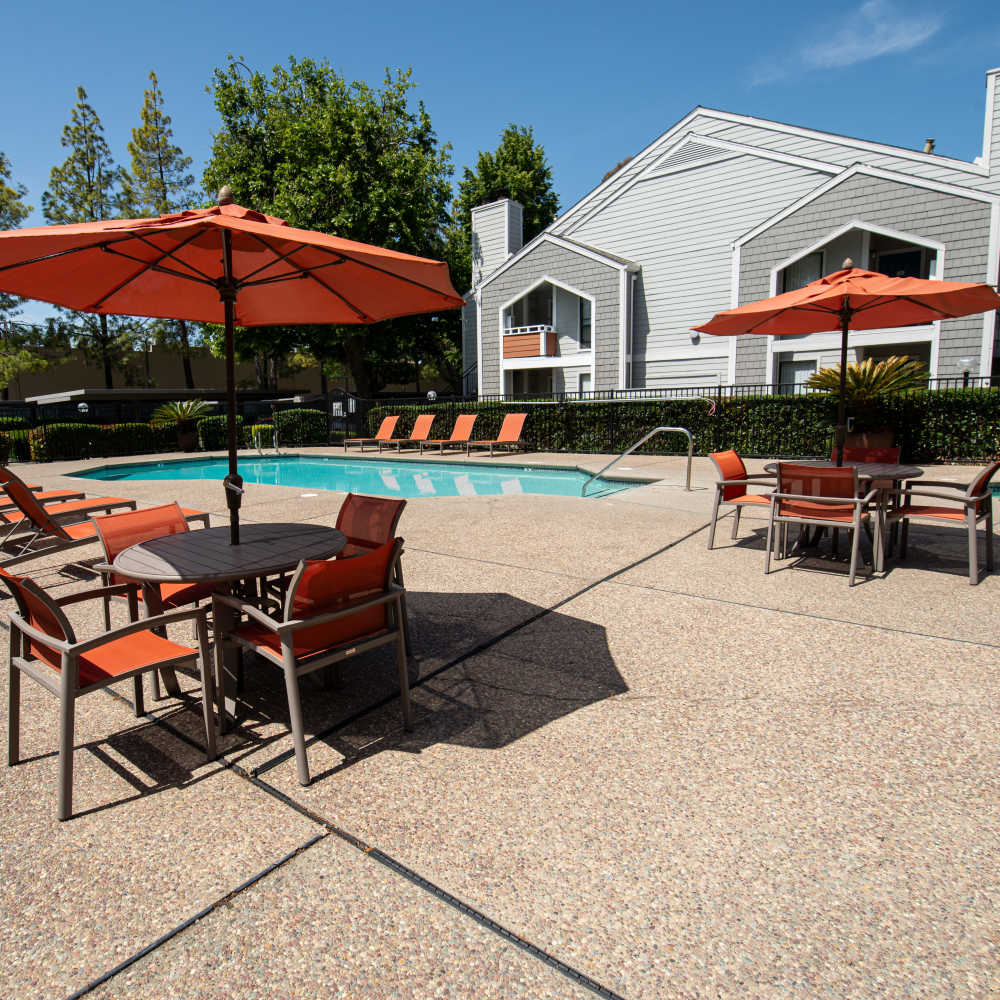 Inviting pool area with shaded tables and lounge chairs at Riverstone Apartment Homes, featuring a clear blue sky at Riverstone Apartments in Sacramento, California