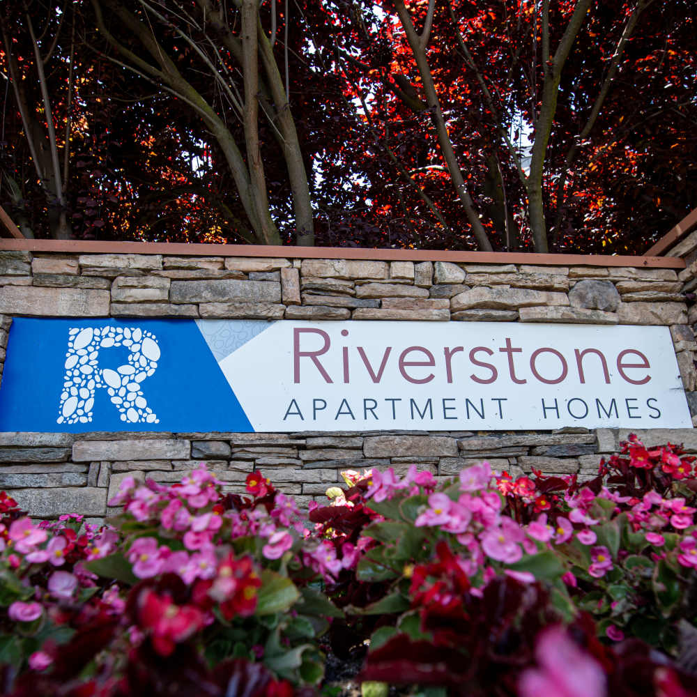 Entrance sign for Riverstone Apartment Homes, framed by vibrant red trees and stonework at Riverstone Apartments in Sacramento, California